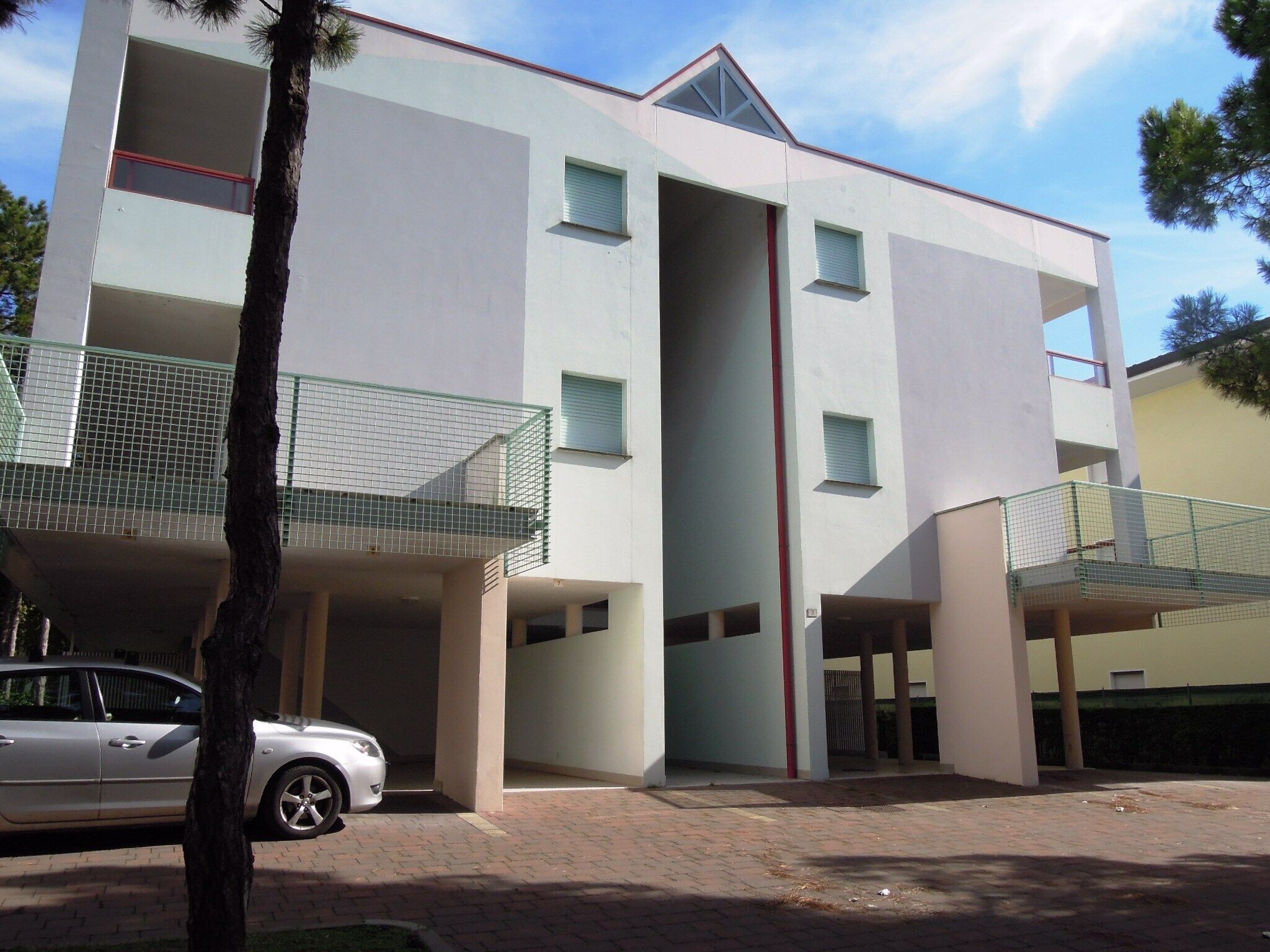 A modern multi-story building with a central vertical corridor, balconies, and a parked car.