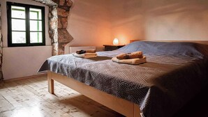 A bedroom with a stone wall, a wooden bed, a nightstand, a lamp, and a window with green shutters. - Holiday home with air conditioning and sea view (Vidovici)