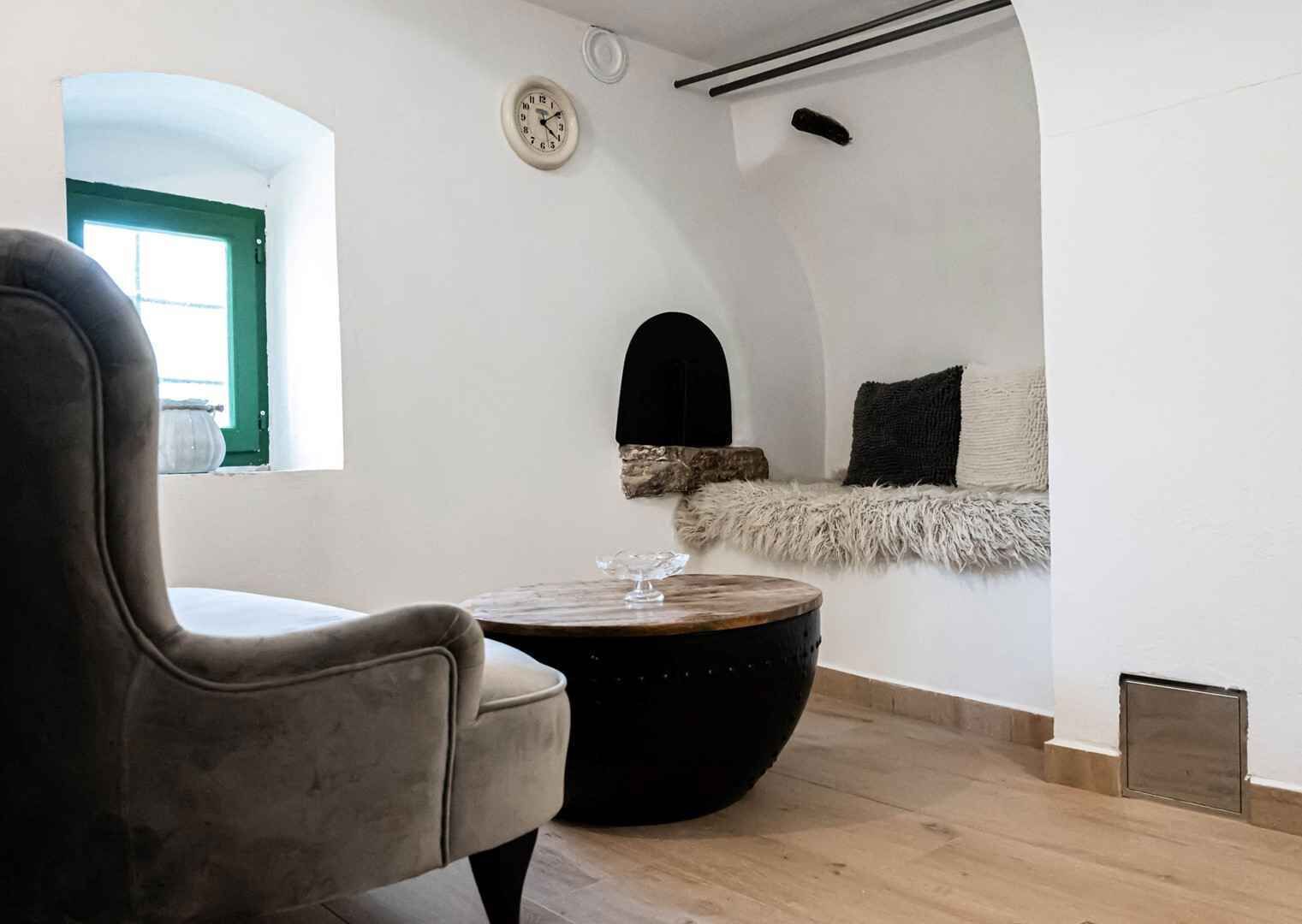 A modern interior with a curved ceiling, a round wooden table, a leather chair, and a small clock on the wall.