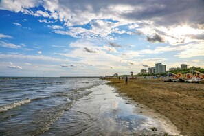 Una playa con olas, una orilla arenosa y edificios al fondo.