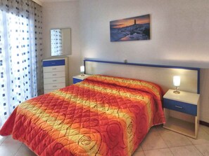 Una habitación de hotel con una cama, una mesita de noche, una cómoda, un cuadro y una ventana con cortinas.
