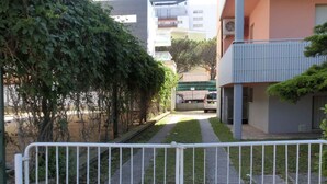 A gated residential area with a white metal fence, a grassy pathway, and multi-story buildings with balconies. - Holiday flat with air conditioning and balcony (Lignano Sabbiadoro)