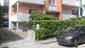 A multi-story residential building with balconies, a car parked in front, and a sign indicating a car park. - Holiday flat with air conditioning and balcony (Lignano Sabbiadoro)