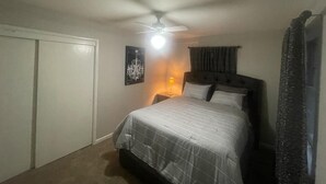 A bedroom with a bed, a ceiling fan, a nightstand, and a wall-mounted lamp. - Stunning 3 bedroom in the heart of dfw (Bedford)