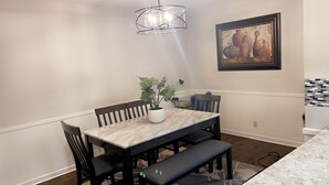 A dining area with a marble table, black chairs, a bench, a potted plant, a pendant light, and a framed artwork on the wall. - Stunning 3 bedroom in the heart of dfw (Bedford)