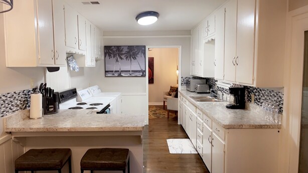 A modern kitchen with white cabinets, a stove, and a microwave. There are two stools and a rug in the center. - Stunning 3 bedroom in the heart of dfw (Bedford)
