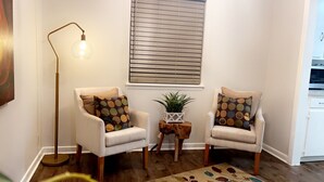 A living room with two armchairs, a floor lamp, a small table with a plant, and a window with blinds. - Stunning 3 bedroom in the heart of dfw (Bedford)