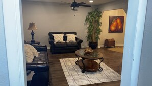 A living room with a dark leather sofa, a glass coffee table, a lamp, a potted plant, and a painting of pears on the wall. - Stunning 3 bedroom in the heart of dfw (Bedford)