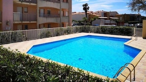 Una piscina rectangular con una escalera metálica en un lateral, rodeada por una valla blanca y abundante vegetación.
