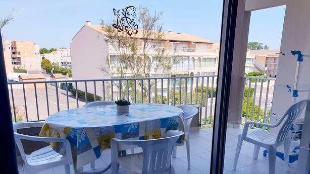 Un balcón con una mesa redonda y sillas, una planta en maceta y vistas de edificios al fondo.