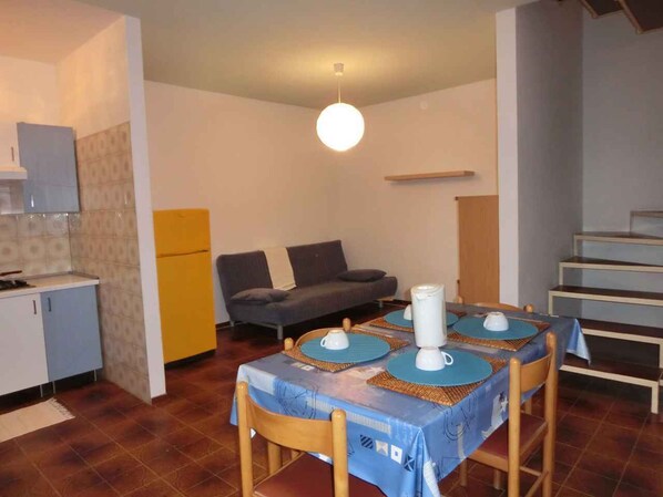 Un comedor con una mesa dispuesta para cuatro personas, un sofá y una cocina al fondo.