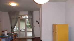 A compact kitchen with a yellow refrigerator, a dining table with chairs, and a sliding glass door leading to an outdoor area. - Holiday apartment with air conditioning, balcony and pool (Bibione)