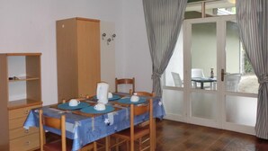 A dining area with a table set for four, a wooden cabinet, and a view through a glass door. - Holiday apartment with air conditioning, balcony and pool (Bibione)