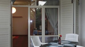A covered patio area with a table and chairs, a sliding glass door leading to an interior space, and a ceiling light fixture. - Holiday apartment with air conditioning, balcony and pool (Bibione)