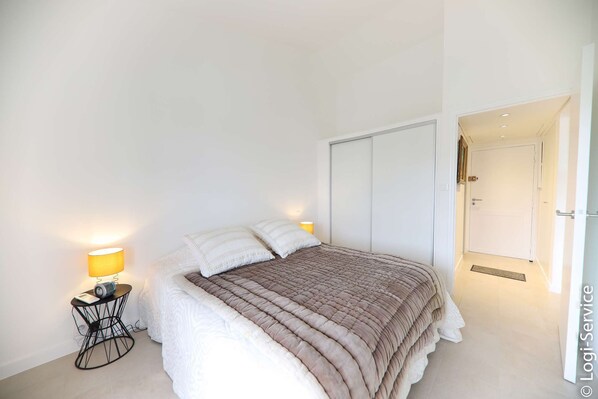 Een slaapkamer met een bed, twee bedlampjes, een nachtkastje en een deur naar een gang.