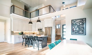 A modern kitchen with white cabinets, a central island with bar stools, a stainless steel refrigerator, and pendant lighting.