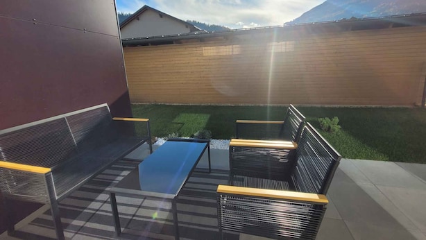 A patio with a glass table and four black metal chairs with wooden armrests. - Holiday apartment new and cozy (Öblarn)