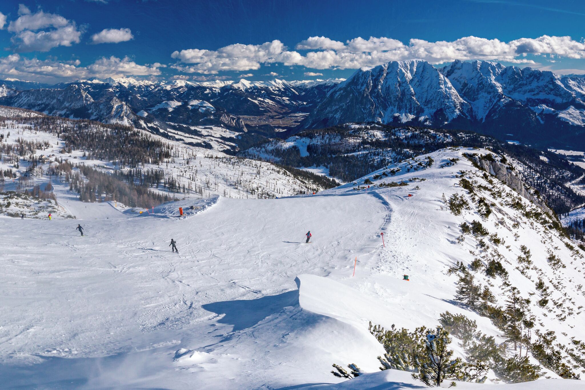 Un paysage de montagne enneigé, avec des skieurs et une vue dégagée sur les montagnes lointaines.