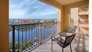 Een balkon met uitzicht op een rivier en gebouwen, ingericht met twee stoelen en een tafel.
