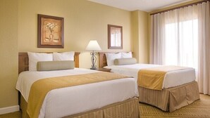 Een hotelkamer met twee bedden, een nachtkastje met een lamp, een lijst met een foto aan de muur en een raam met gordijnen.