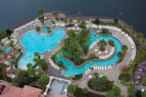 Luchtbeeld van een resort met meerdere zwembaden, ligbedden en palmbomen.