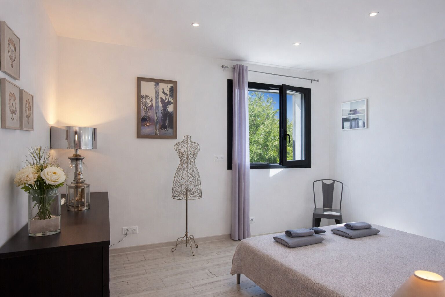 A bedroom with a bed, a chair, a mannequin, a window, and artwork on the walls.