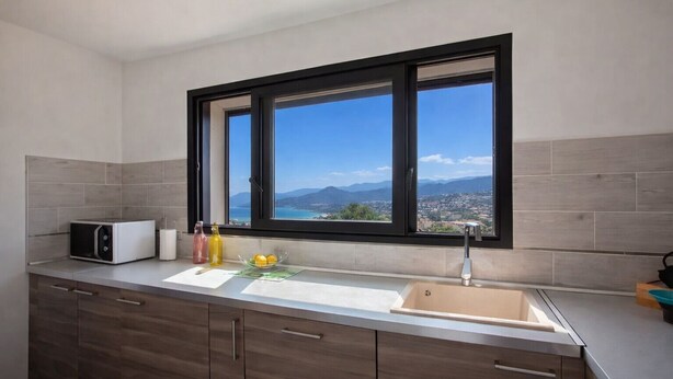 A modern kitchen with a large window, a microwave, a sink, and wooden cabinets. - Casa Bianca (L'Île-Rousse)