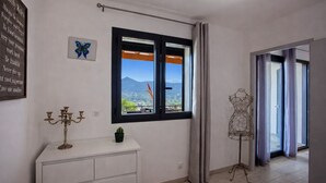 A room with a large window, a white dresser, a cactus, a butterfly art piece, and a mannequin. - Casa Bianca (L'Île-Rousse)