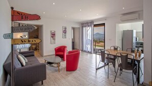 A modern living room with a sofa, red chairs, a dining table, and a kitchen area. - Casa Bianca (L'Île-Rousse)