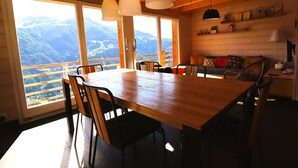A wooden interior with a large dining table, chairs, and a sofa. There are large windows with a mountain view. - Outside: Detached chalet on 3 floors with magnificent views, for 4 people - approx. 80m2Inside: Brig (St-Luc)