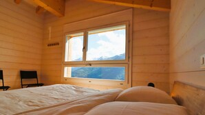 A wooden cabin bedroom with two beds, a window with a mountain view, and a chair. - Outside: Detached chalet on 3 floors with magnificent views, for 4 people - approx. 80m2Inside: Brig (St-Luc)