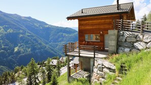 A wooden cabin with a stone foundation, a balcony, and a view of a mountainous landscape. - Outside: Detached chalet on 3 floors with magnificent views, for 4 people - approx. 80m2Inside: Brig (St-Luc)