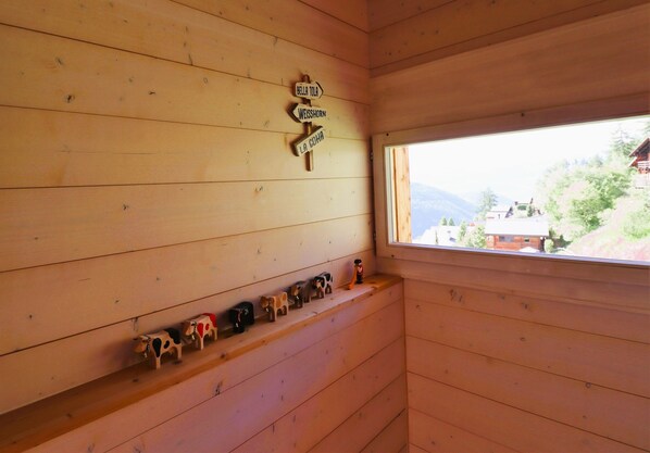 L’intérieur d’un chalet en bois, avec une fenêtre donnant sur le paysage, une étagère ornée de figurines de vaches et un panneau indicateur.