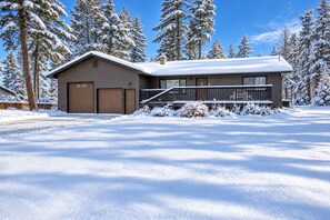 A two-story house with a garage, surrounded by snow-covered trees.