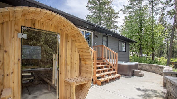 A wooden hot tub with a wooden staircase leading to a deck, surrounded by a stone wall and a wooden deck.