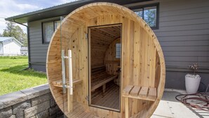 A wooden sauna with a bench inside, a glass door, and a stone wall outside.
