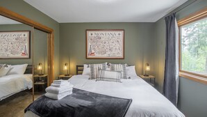 A hotel room with a large bed, two bedside tables with lamps, a mirror, a map of Montana on the wall, and a window with curtains.