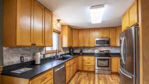A kitchen with wooden cabinets, stainless steel appliances, a black countertop, and a stone backsplash.