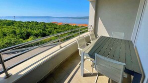 Een balkon met een tafel en stoelen, met uitzicht op een kustlandschap met bomen en gebouwen.