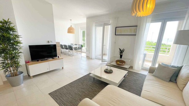 Een moderne woonkamer met een bank, salontafel, televisie en een eethoek.