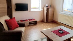 Un salon avec un canapé, un téléviseur, un meuble en bois et une fenêtre.