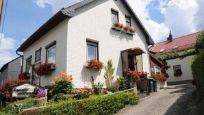 Un bâtiment blanc avec un toit en pente, de nombreuses fenêtres et des jardinières au deuxième étage.