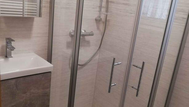 Ein modernes Badezimmer mit einer gläsernen Duschkabine, einem weißen Waschbecken und einer Marmorarbeitsplatte.