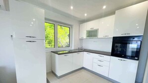A modern kitchen with white cabinetry, a built-in oven, and a window providing natural light. - Villa with great views and jacuzzi (Crikvenica)