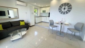 A modern living room with a black sofa, a glass coffee table, and a dining area with two chairs and a table. A large wall clock is visible. - Villa with great views and jacuzzi (Crikvenica)