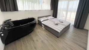 A modern bedroom with a large bed, a black bathtub, and large windows with sheer curtains. - Villa with great views and jacuzzi (Crikvenica)
