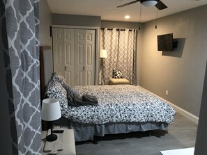 A bedroom with a bed, a nightstand, a lamp, a chair, a TV, and a ceiling fan.