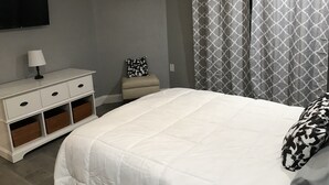 Ein Schlafzimmer mit einem Bett, einem Nachttisch, einer Lampe, einem Sessel und einem an der Wand befestigten Fernseher.