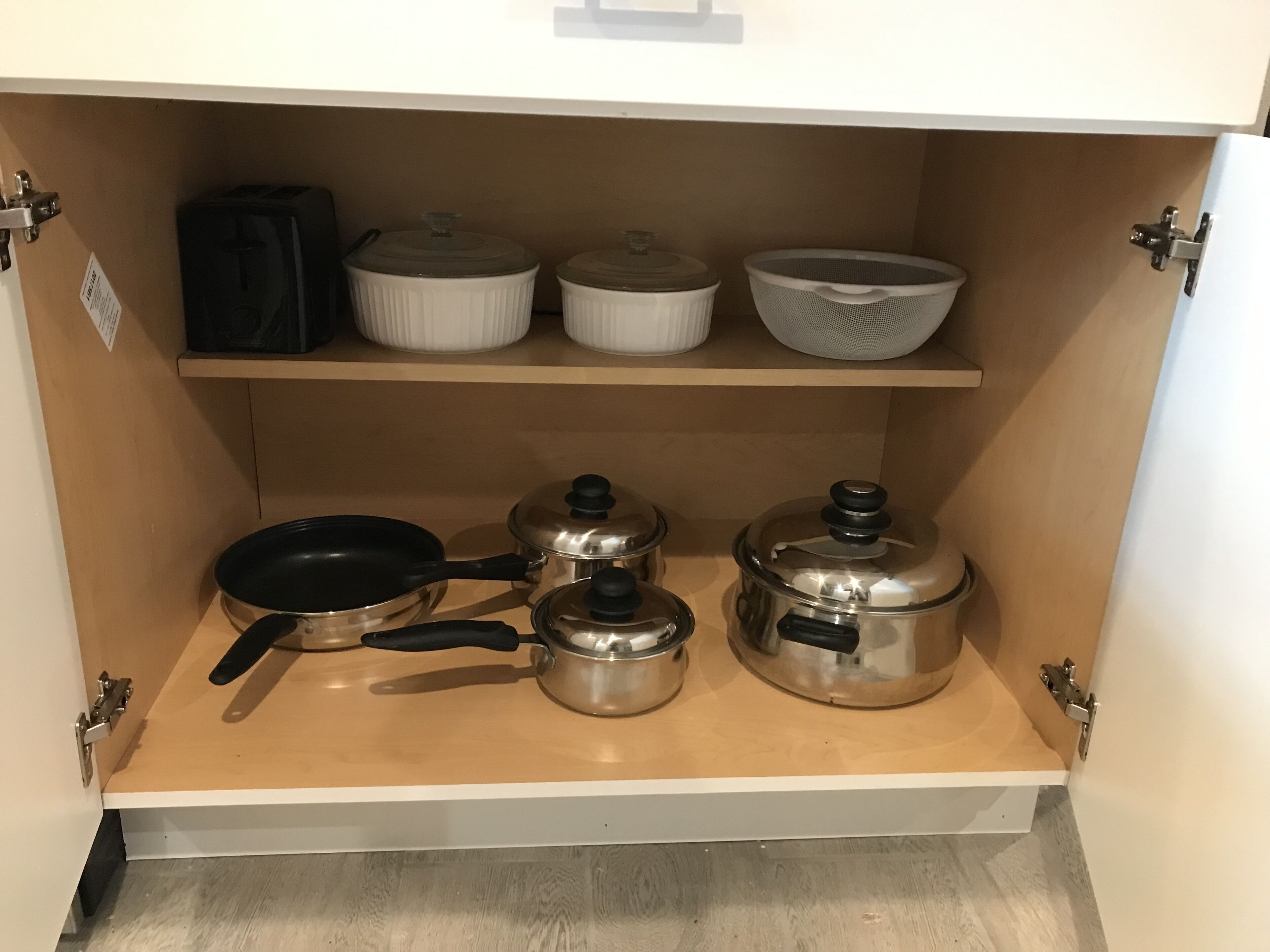 A kitchen cabinet with cookware and storage containers.