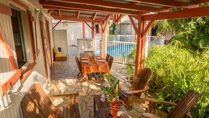 A covered patio with a pool, wooden furniture, and tropical plants. - Gîte Ixora 4/6 pers in the residence Les Jardins de Pointe Noire, swimming pool (pointe noire)